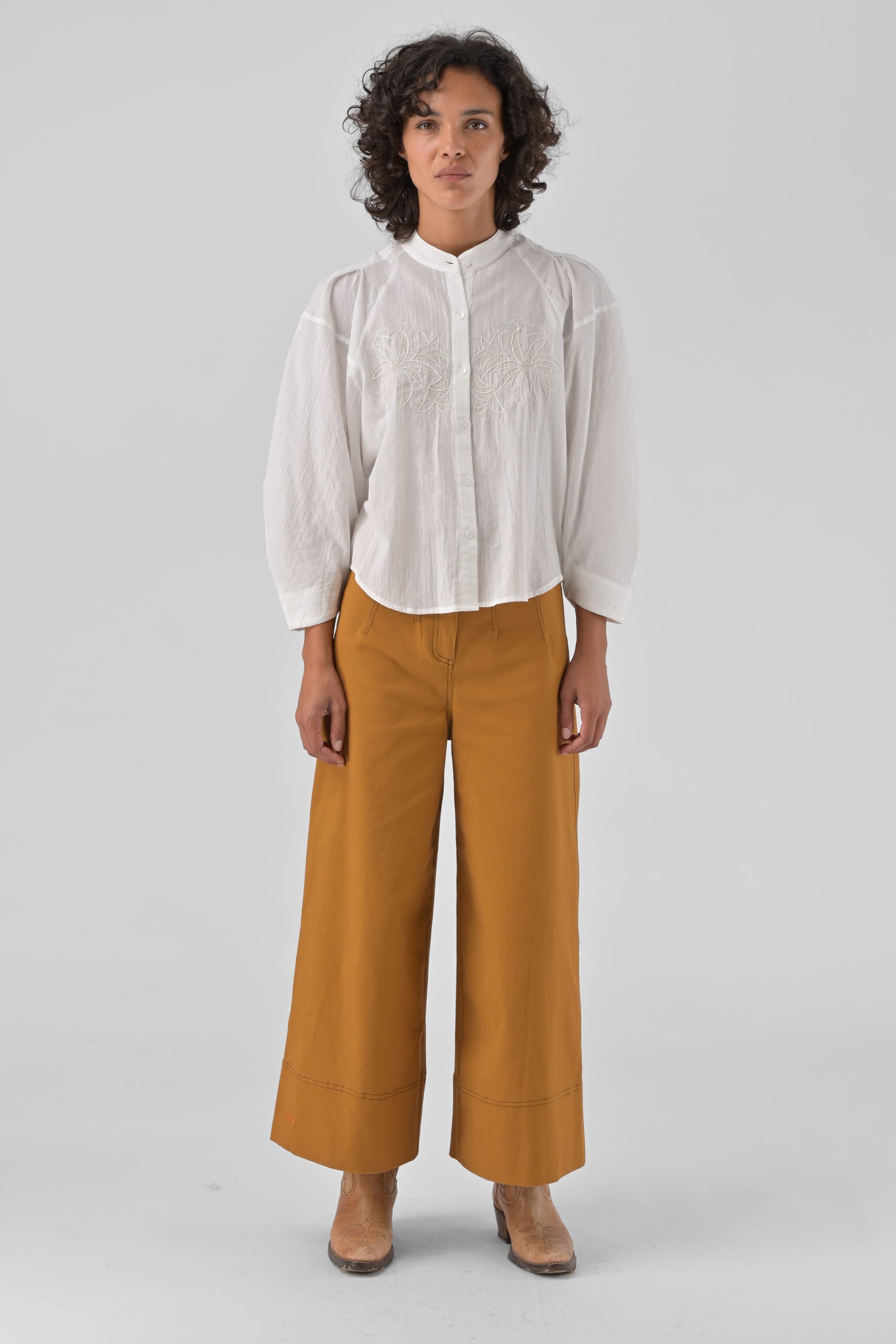 Person wearing a white shirt and mustard yellow pants on a light gray background