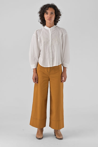 Person wearing a white shirt and mustard yellow pants on a light gray background