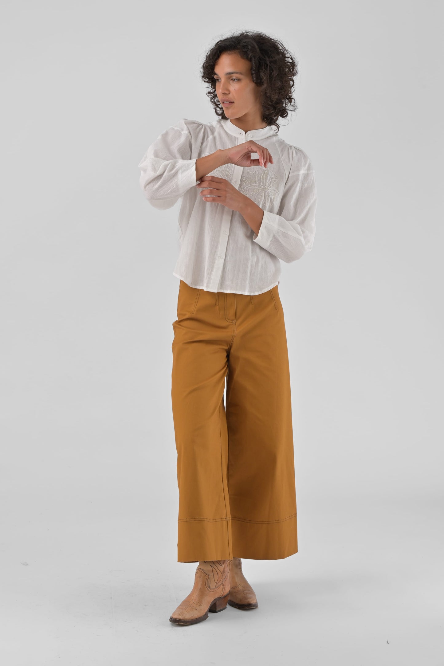 Person wearing a white shirt and mustard yellow pants on a light gray background
