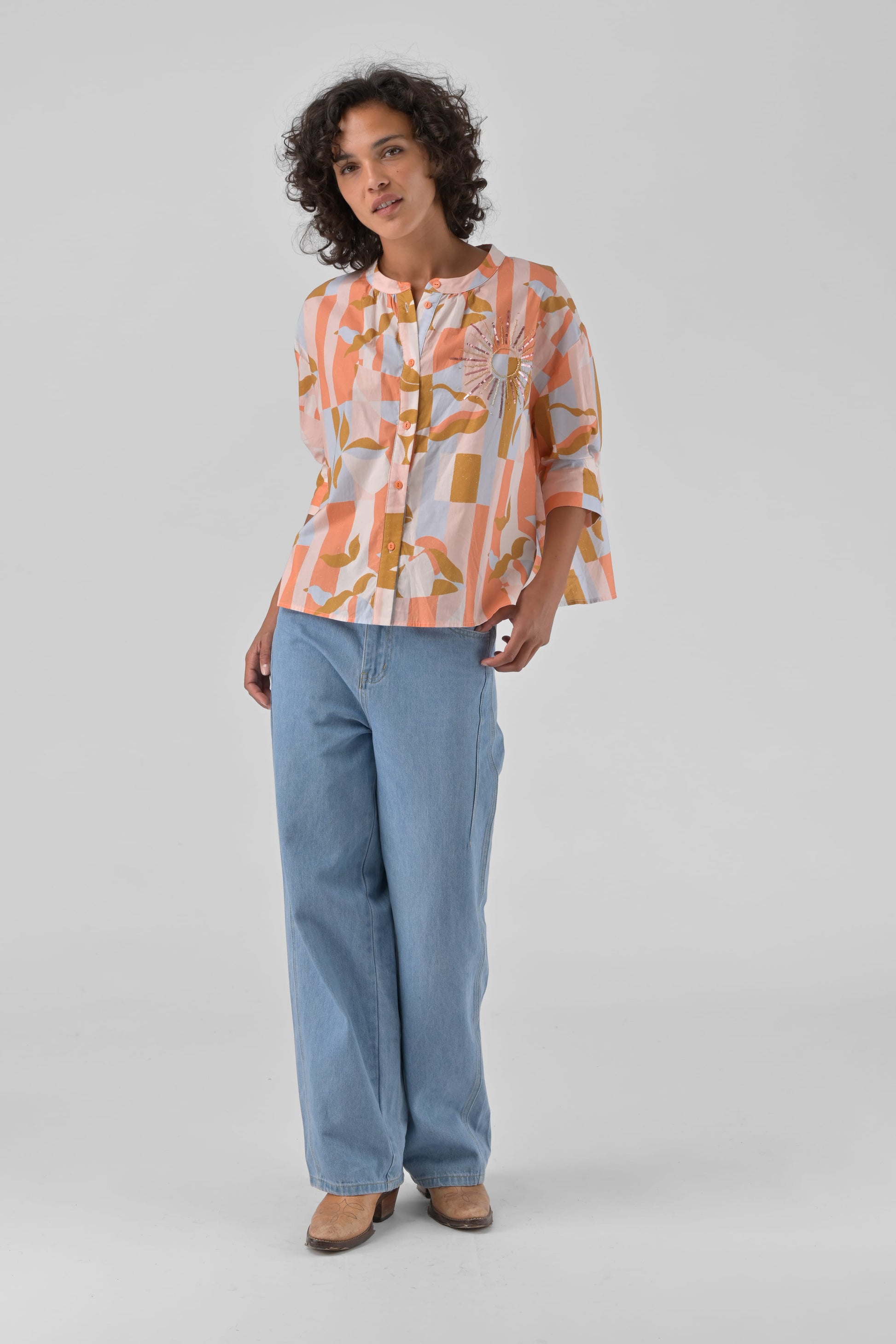 Woman wearing a patterned blouse and light blue jeans on a gray background