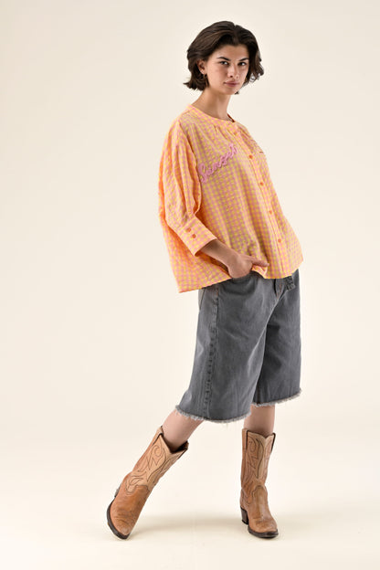 Woman wearing an orange checkered shirt, gray skirt, and brown boots on a beige background