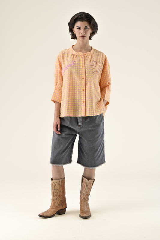 Person wearing an orange checkered shirt, gray shorts, and brown boots on a white background
