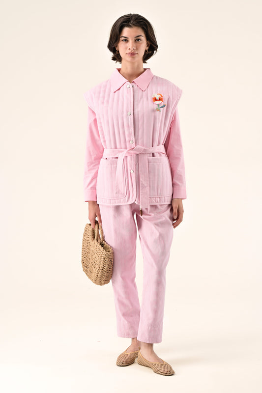 Woman wearing a pink outfit with a belt and holding a straw bag on a white background