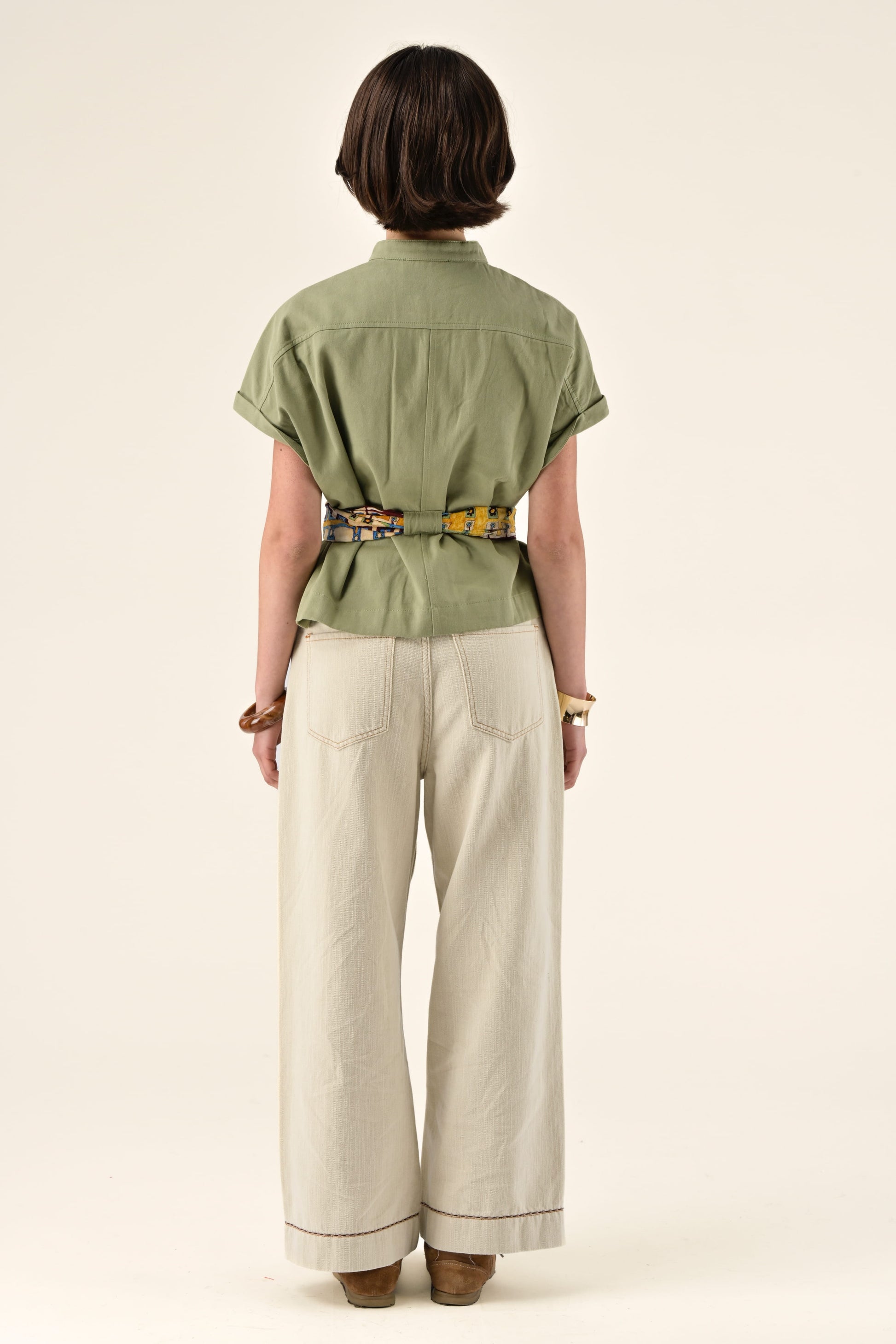 Person wearing a green shirt and beige pants on a white background