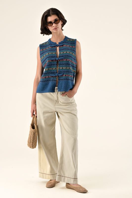 Woman wearing a blue patterned sleeveless top and beige pants on a white background