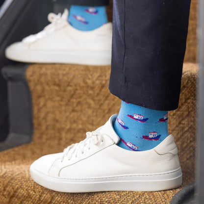Person wearing white sneakers and blue socks with boat design on a carpeted floor.