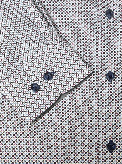 Close-up of a patterned shirt fabric with a repeating small geometric motif in red, white, and dark blue, plus matching dark buttons and a diagonal fold.