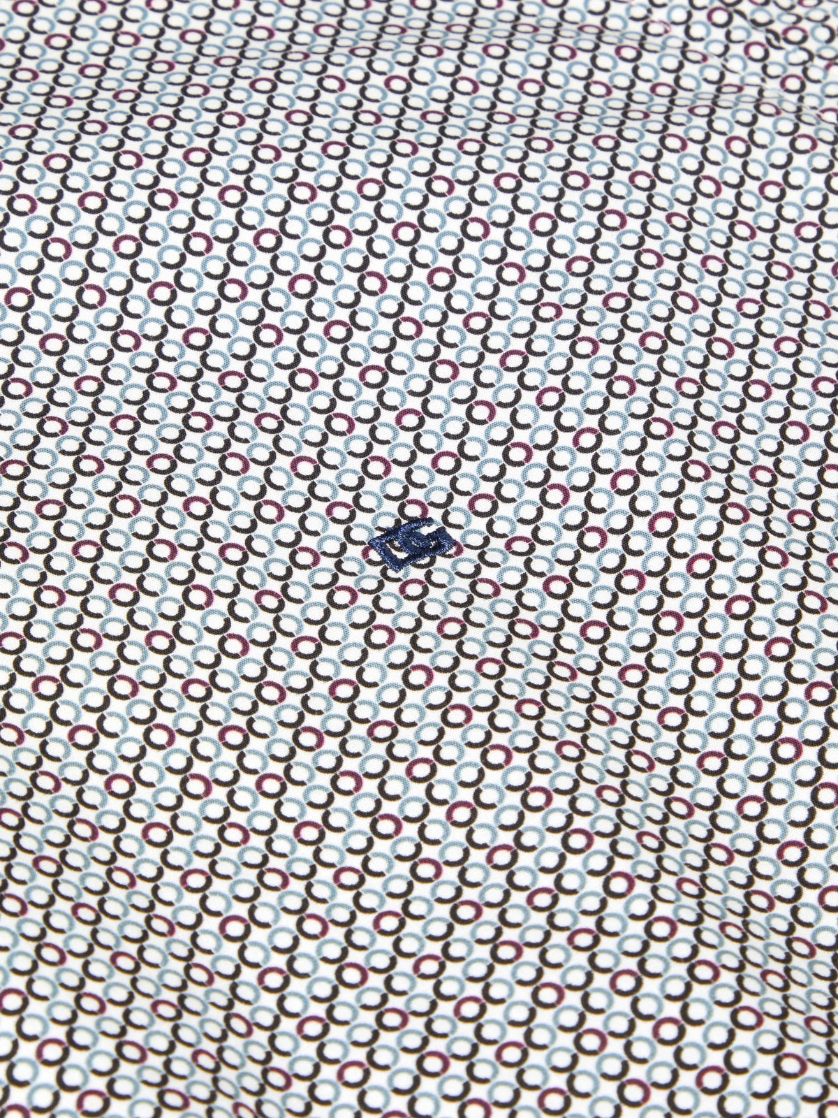 A close-up of a white fabric with a repeating geometric pattern of interlocking circles in brown, red, and light blue, featuring a small dark blue logo in the center.