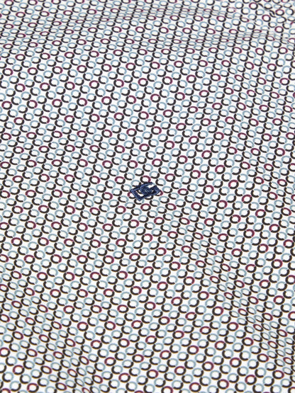 A close-up of a white fabric with a repeating geometric pattern of interlocking circles in brown, red, and light blue, featuring a small dark blue logo in the center.