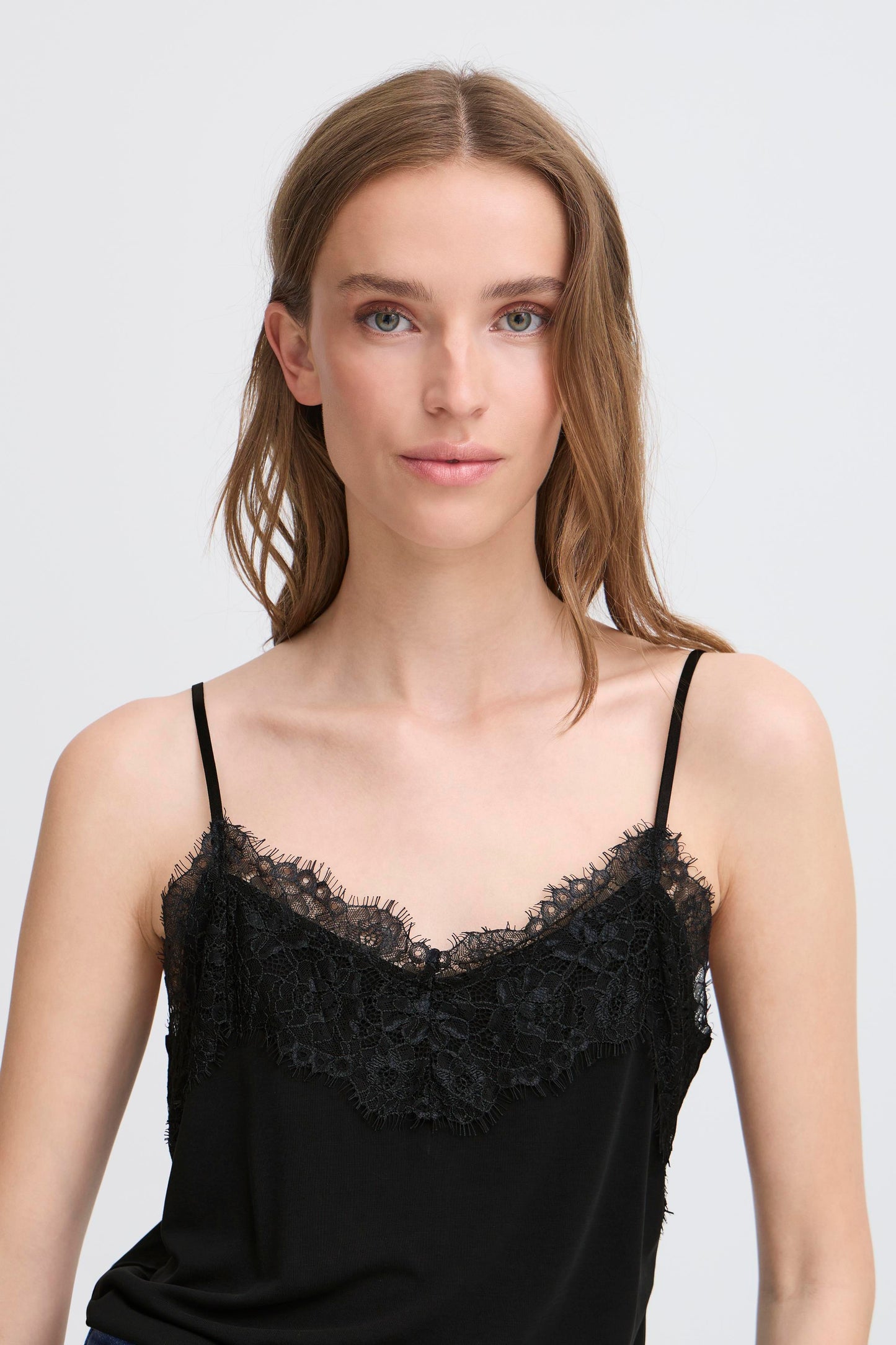 Woman wearing a black lace-trimmed top against a plain background