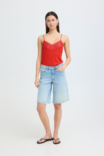 Woman wearing a red lace camisole and light blue denim shorts on a white background
