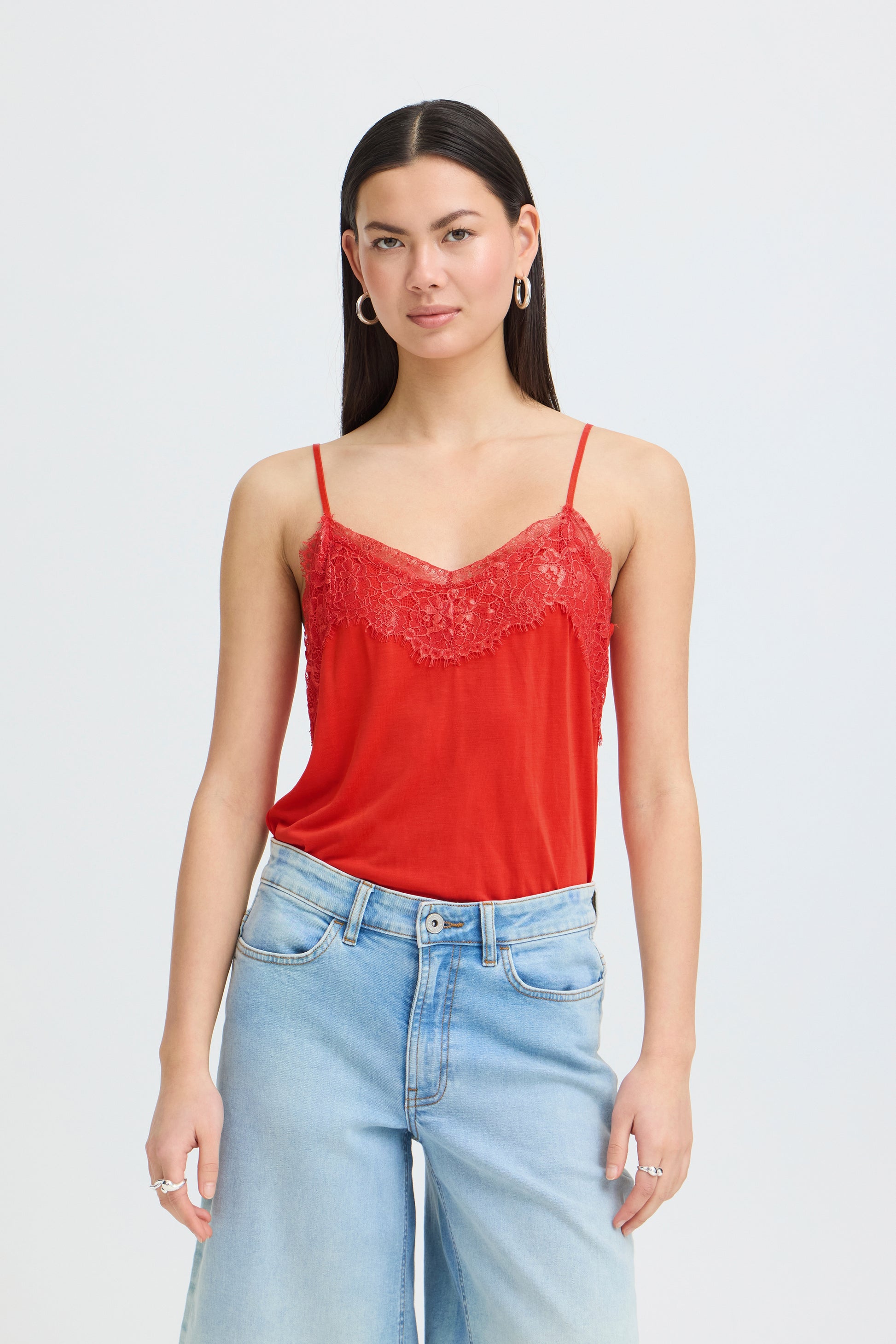 Woman wearing a red lace-trimmed top and light blue jeans on a white background