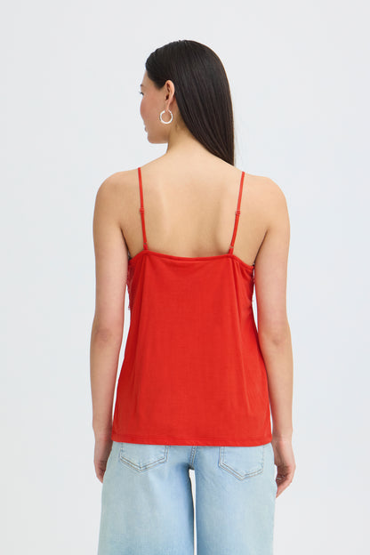 Woman wearing a red spaghetti strap top and light blue jeans on a white background