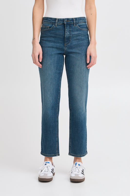Person wearing blue jeans and white sneakers on a plain background