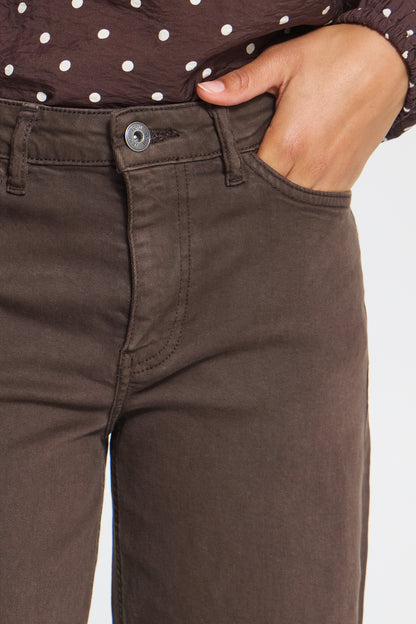 Close-up of a person wearing dark brown straight-leg jeans, with a hand in the pocket and a brown polka-dot top visible at the waist.