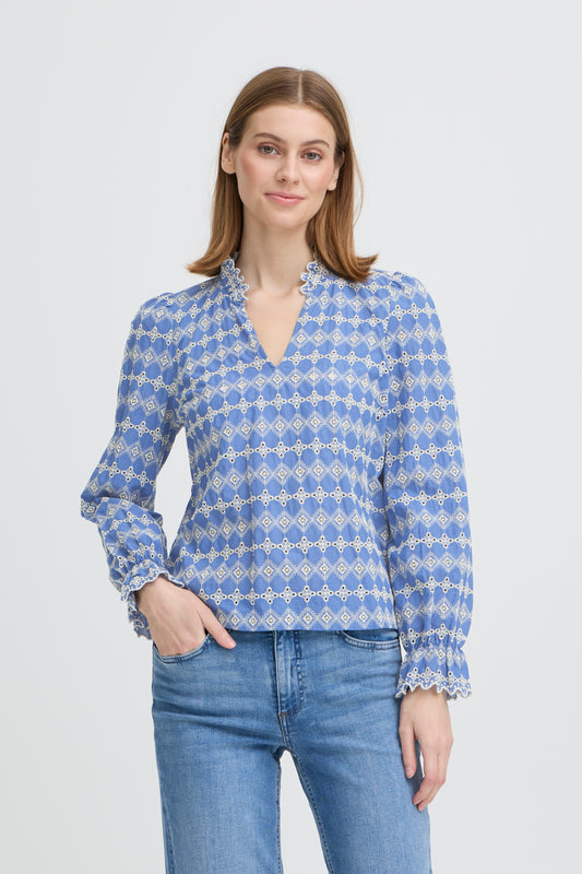 Woman wearing a blue patterned blouse and jeans on a white background