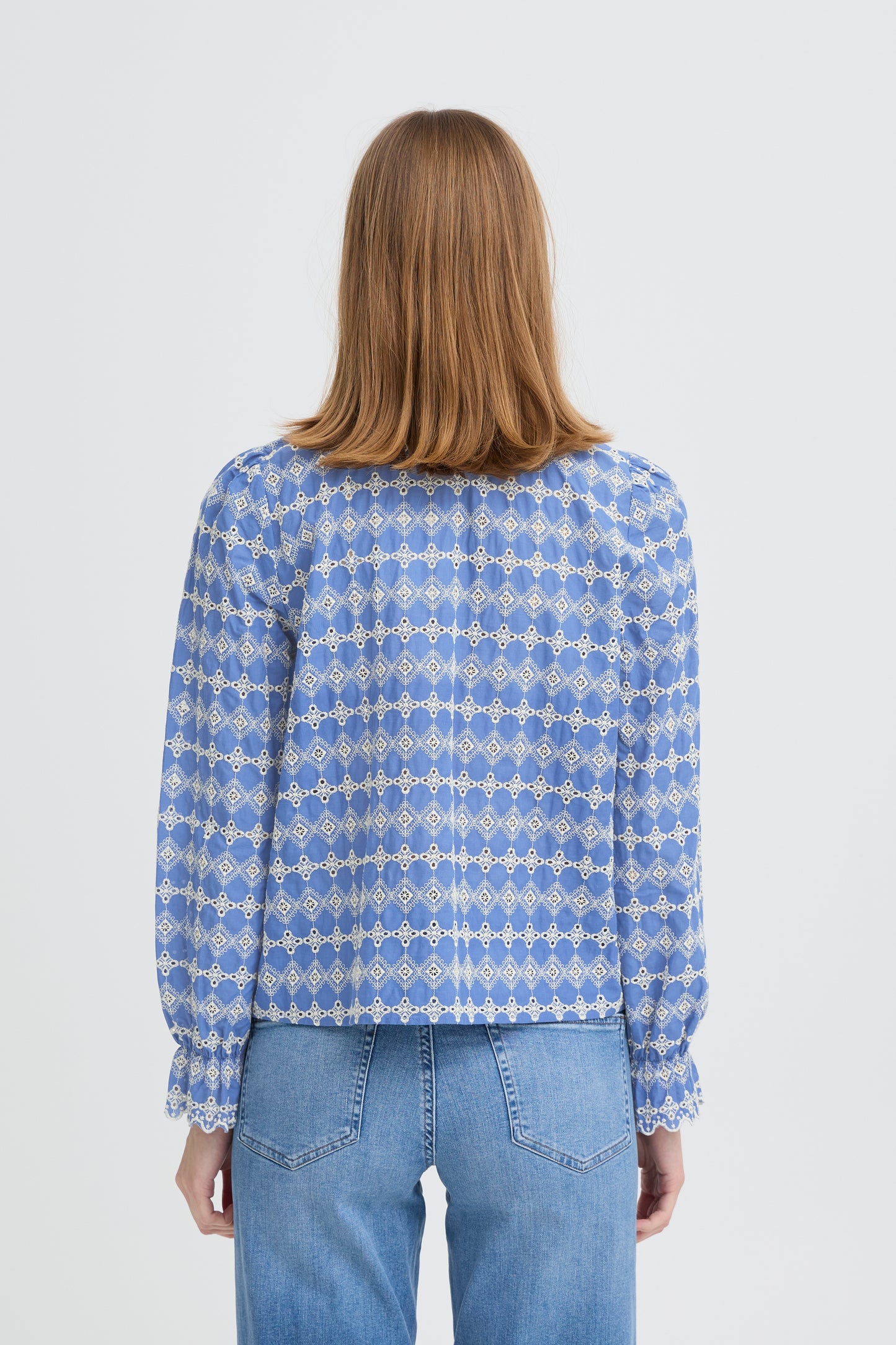 Person wearing a blue patterned blouse and jeans on a white background