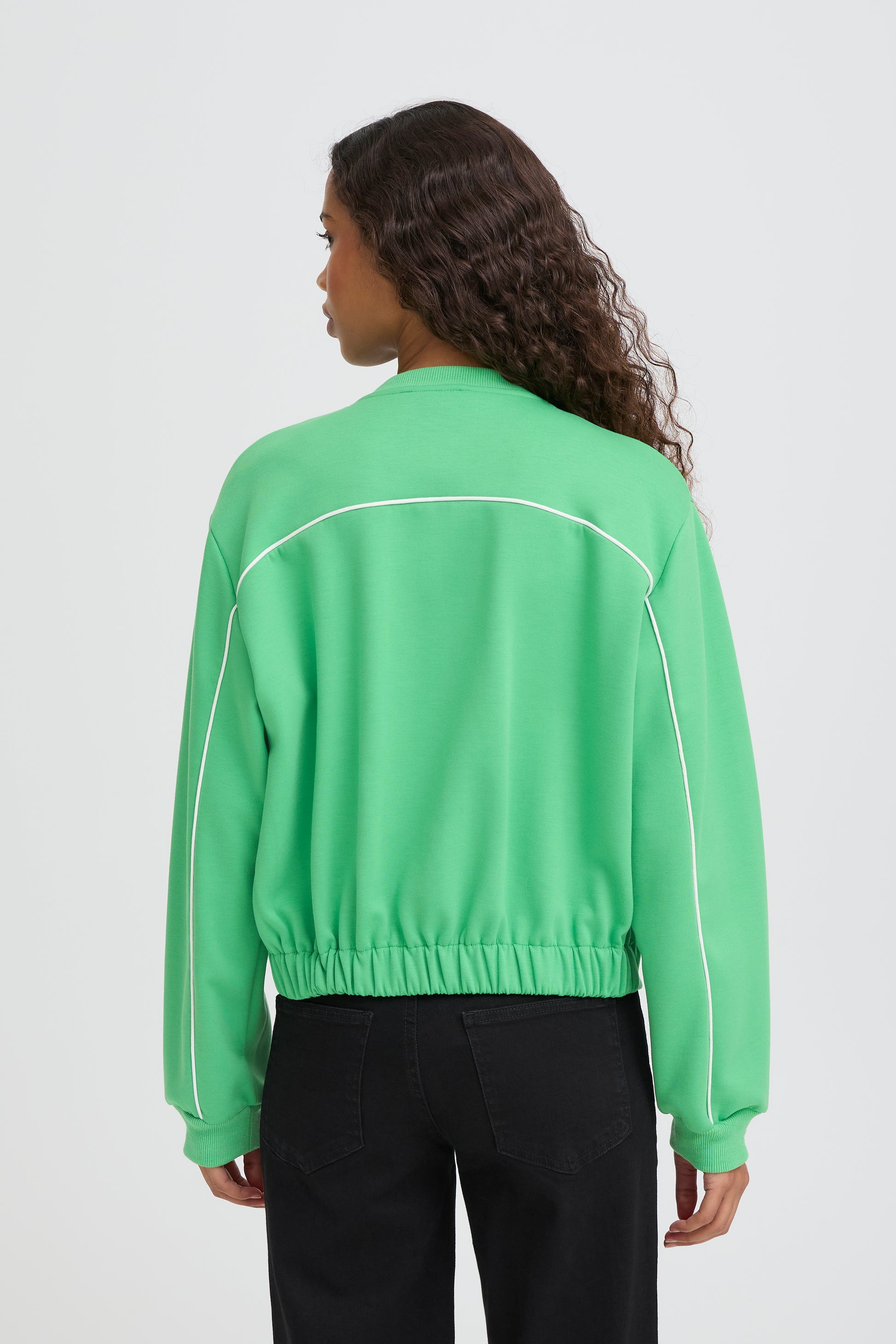 Person wearing a green jacket with white accents on a plain background
