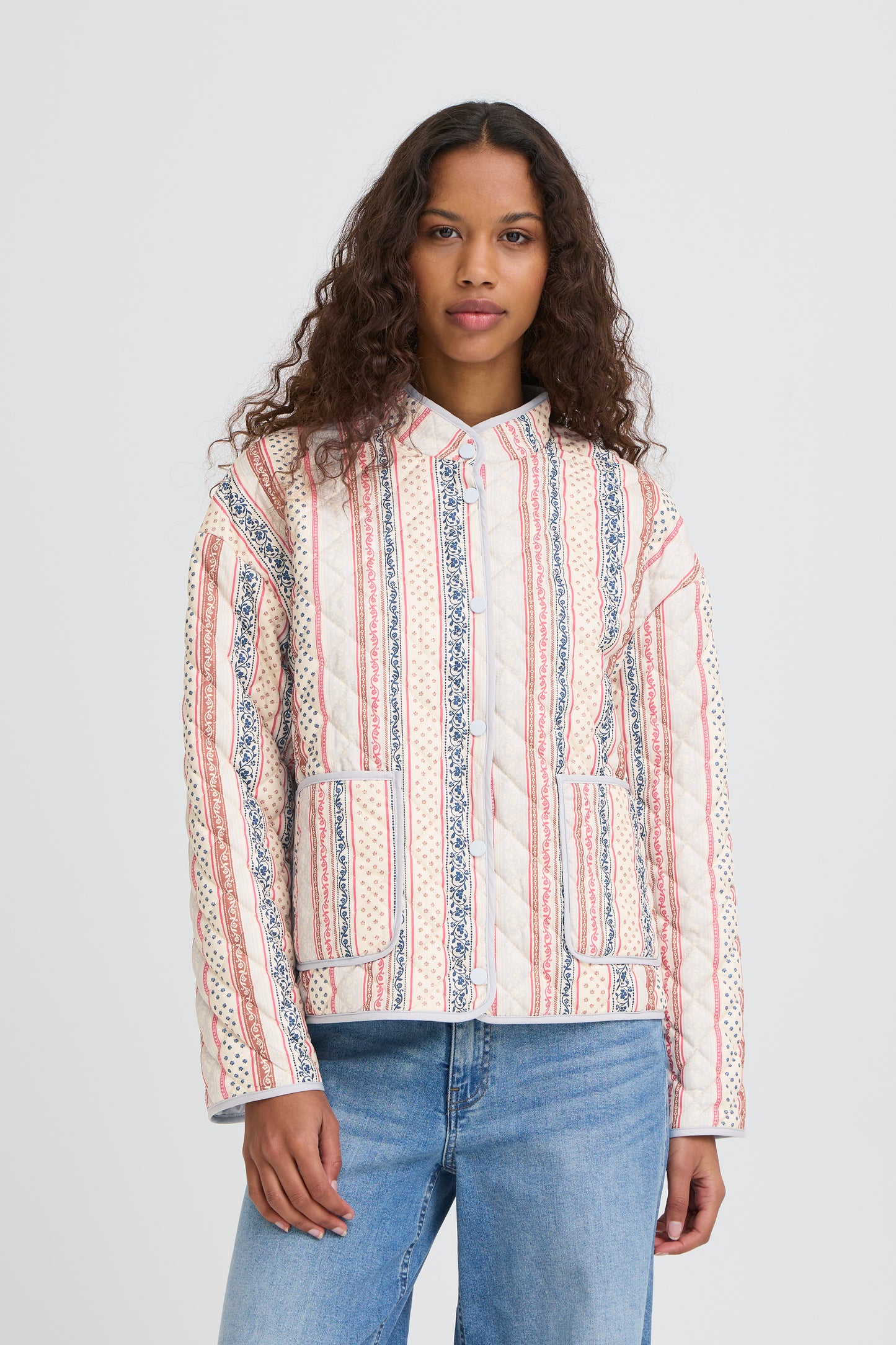 Woman wearing a patterned shirt and jeans on a plain background