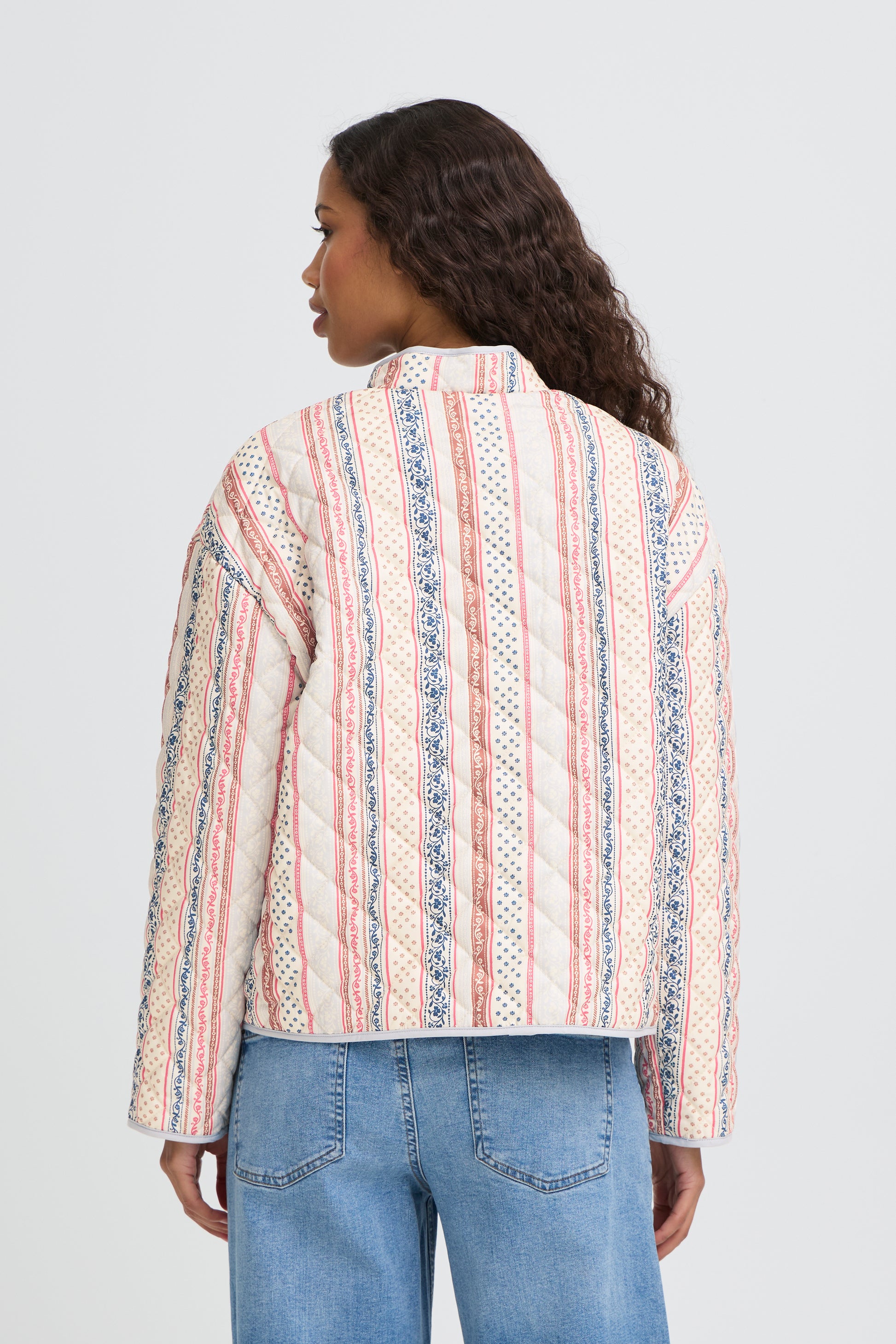 Woman wearing a patterned shirt and jeans on a white background