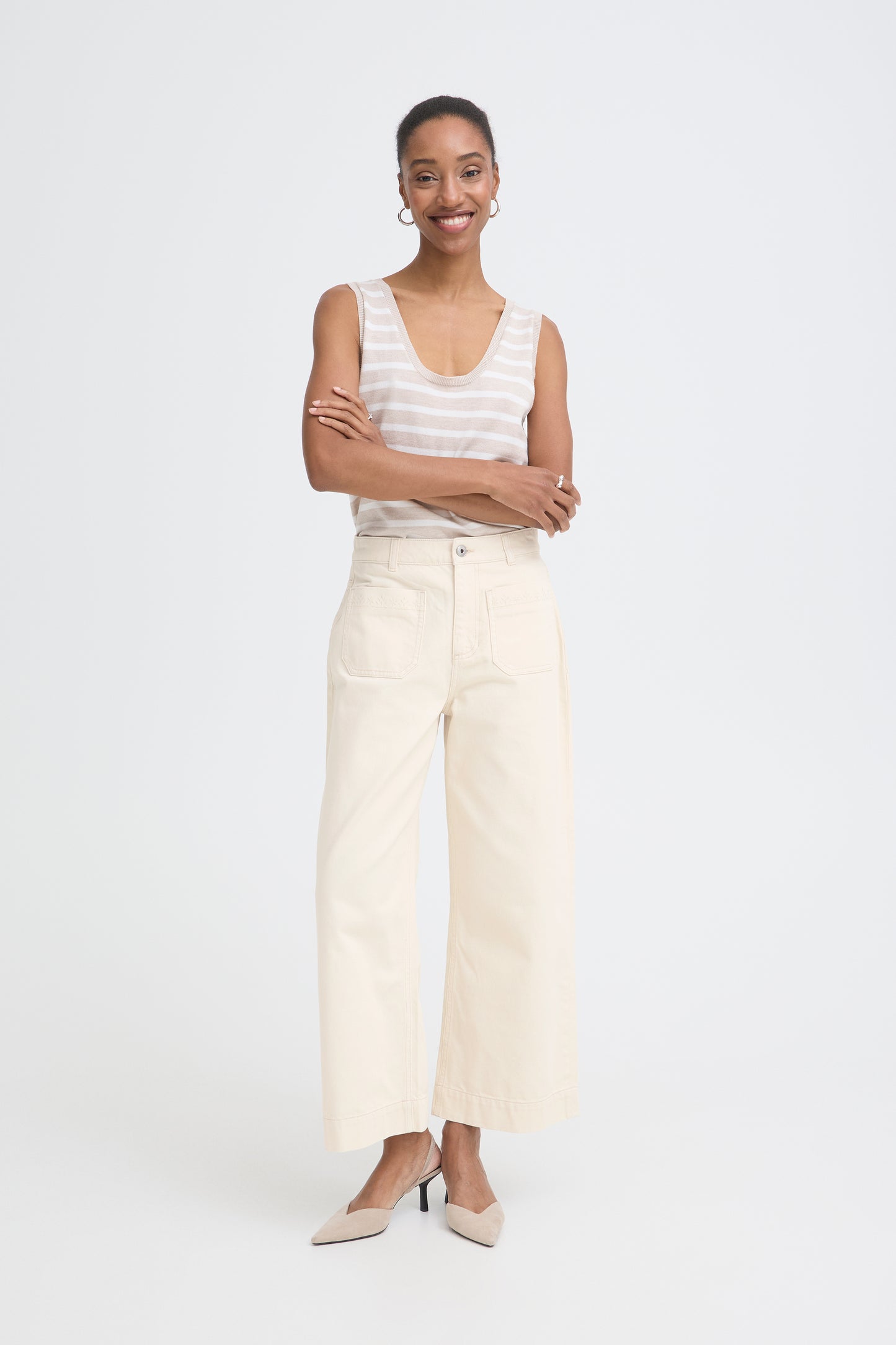 Woman wearing a white sleeveless top and beige pants on a white background