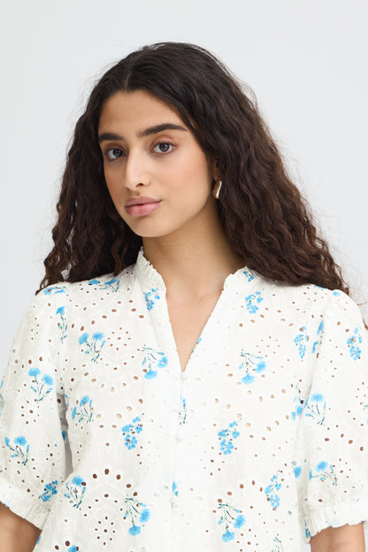 Woman wearing a white blouse with blue floral patterns against a plain background