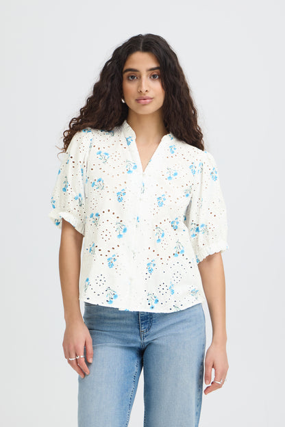Woman wearing a white blouse with blue floral patterns and light blue jeans on a plain background