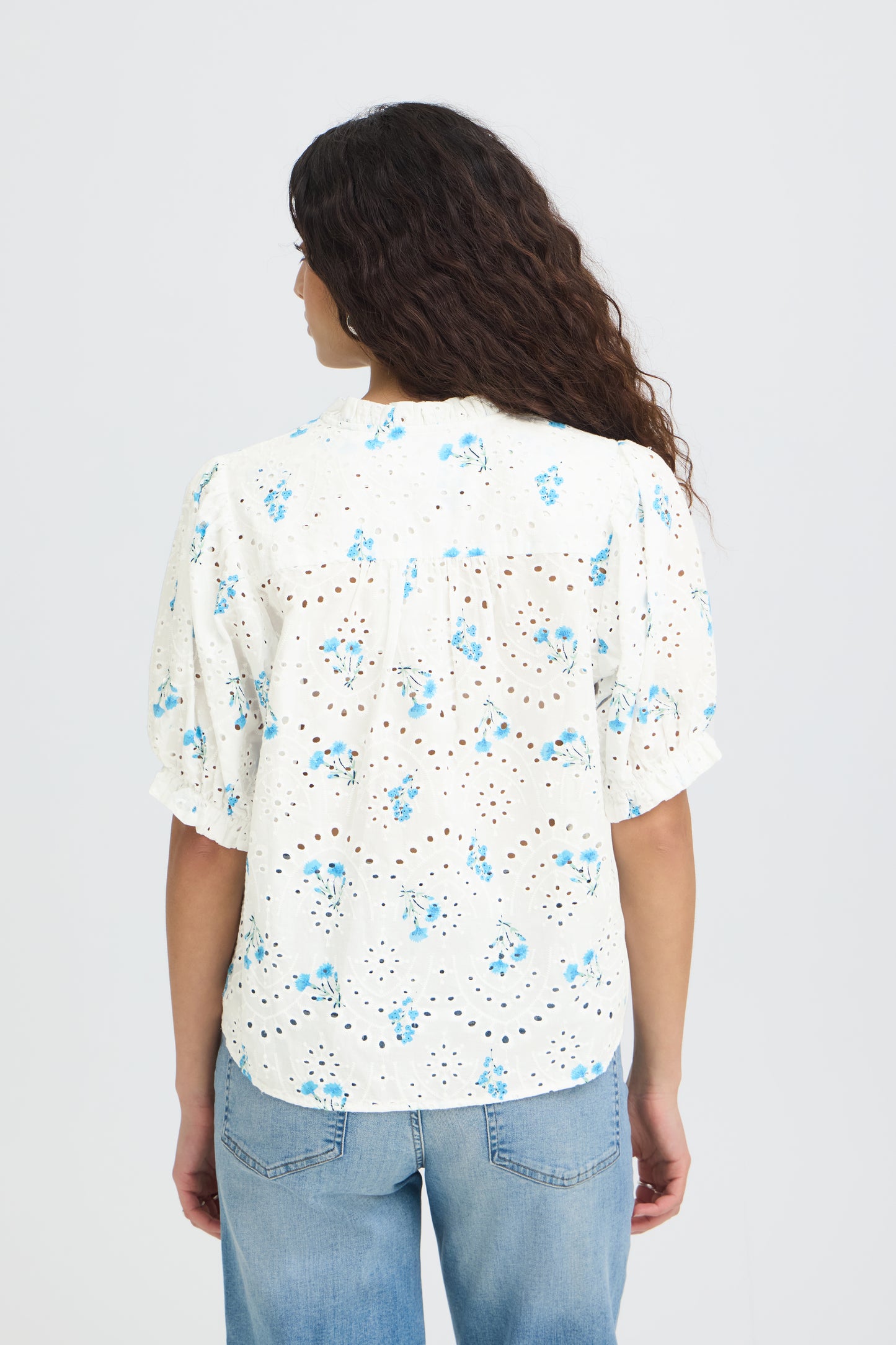 Woman wearing a white floral blouse with blue flowers on a plain background