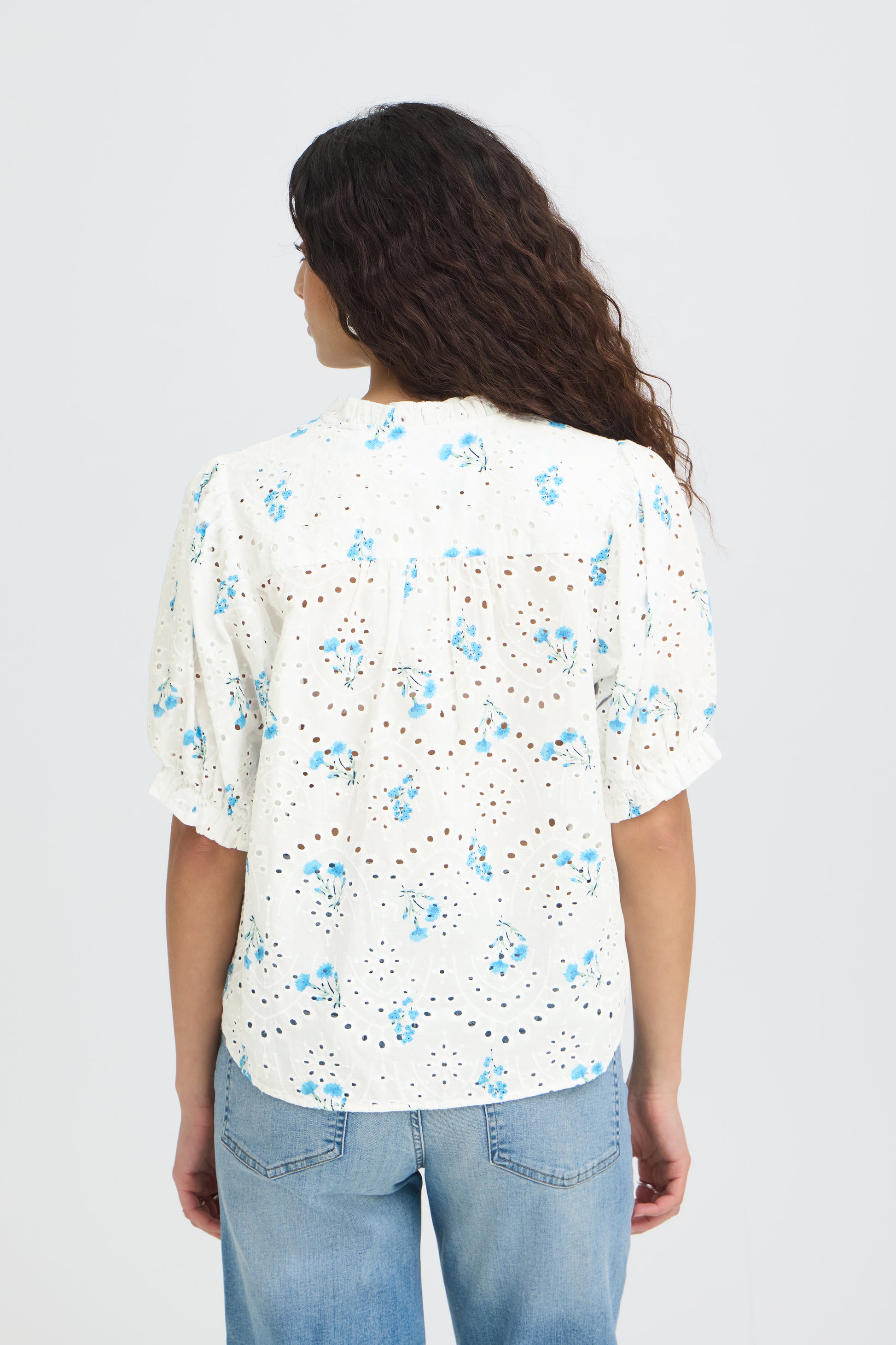 Woman wearing a white floral blouse with blue flowers on a plain background