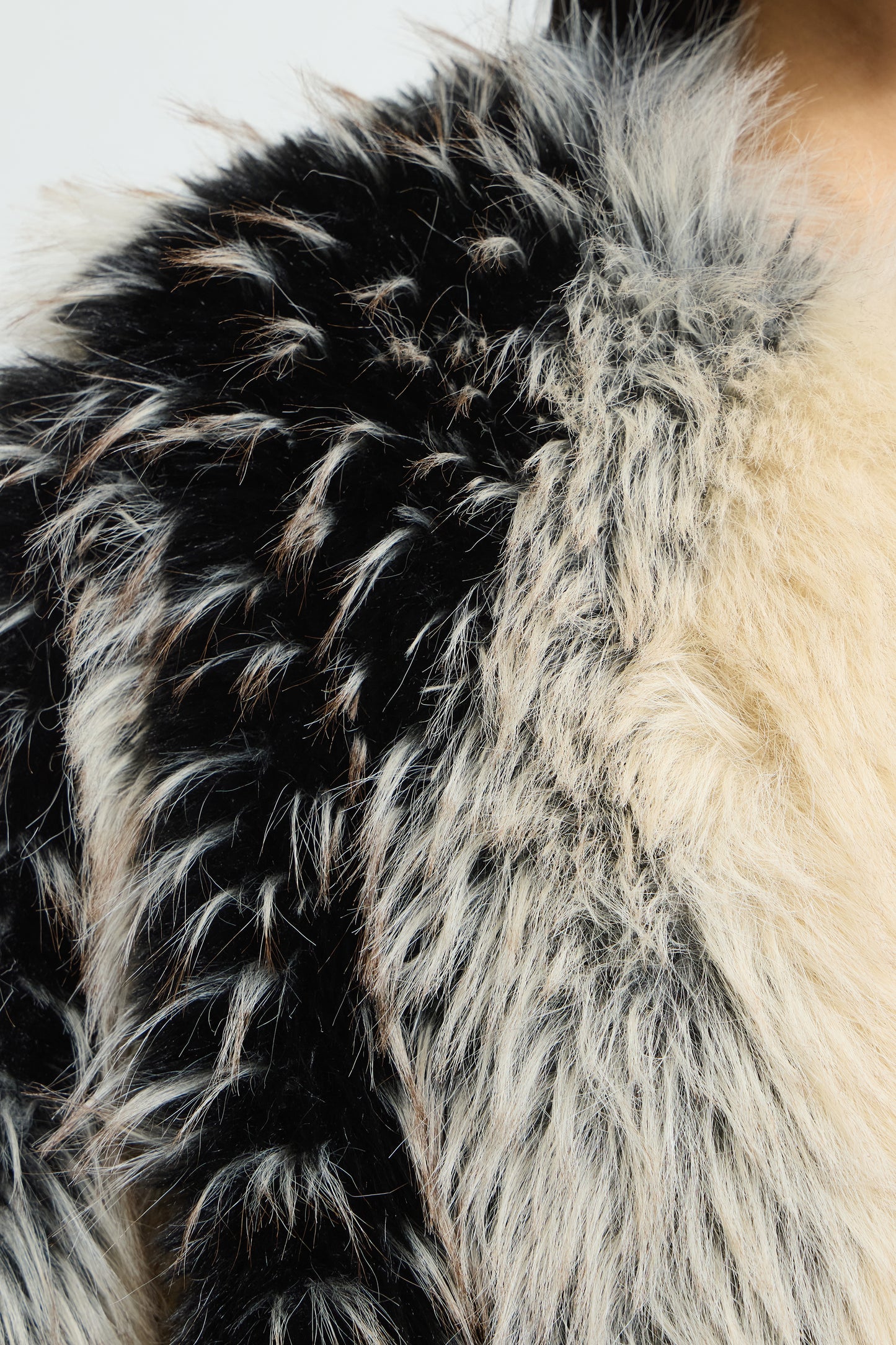 Close-up of a faux fur garment showing a mix of black, white, and cream-colored fluffy texture.
