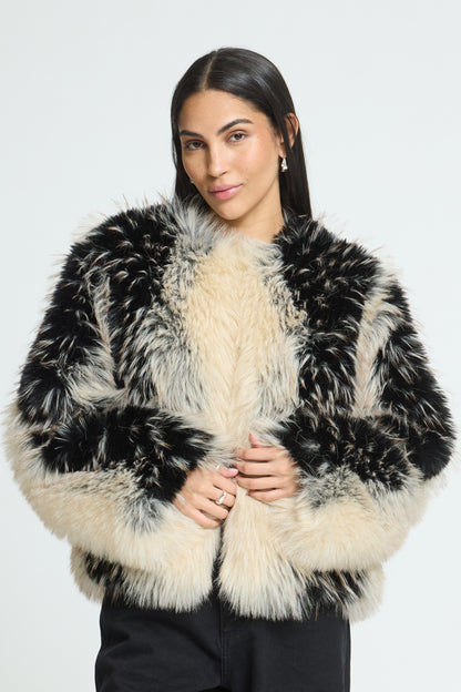 A woman modeling a black and cream mottled fur jacket against a plain light gray studio background.