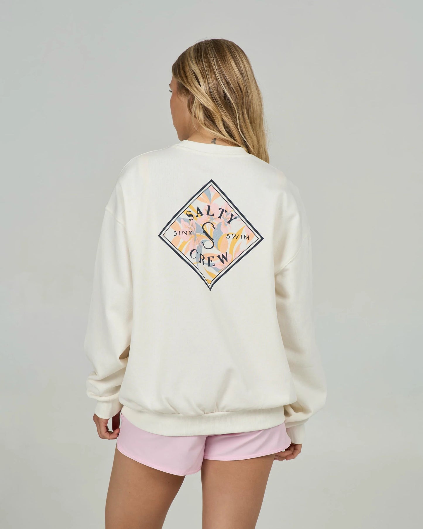 Person wearing a cream sweatshirt with a colorful logo on the back, standing against a plain background.