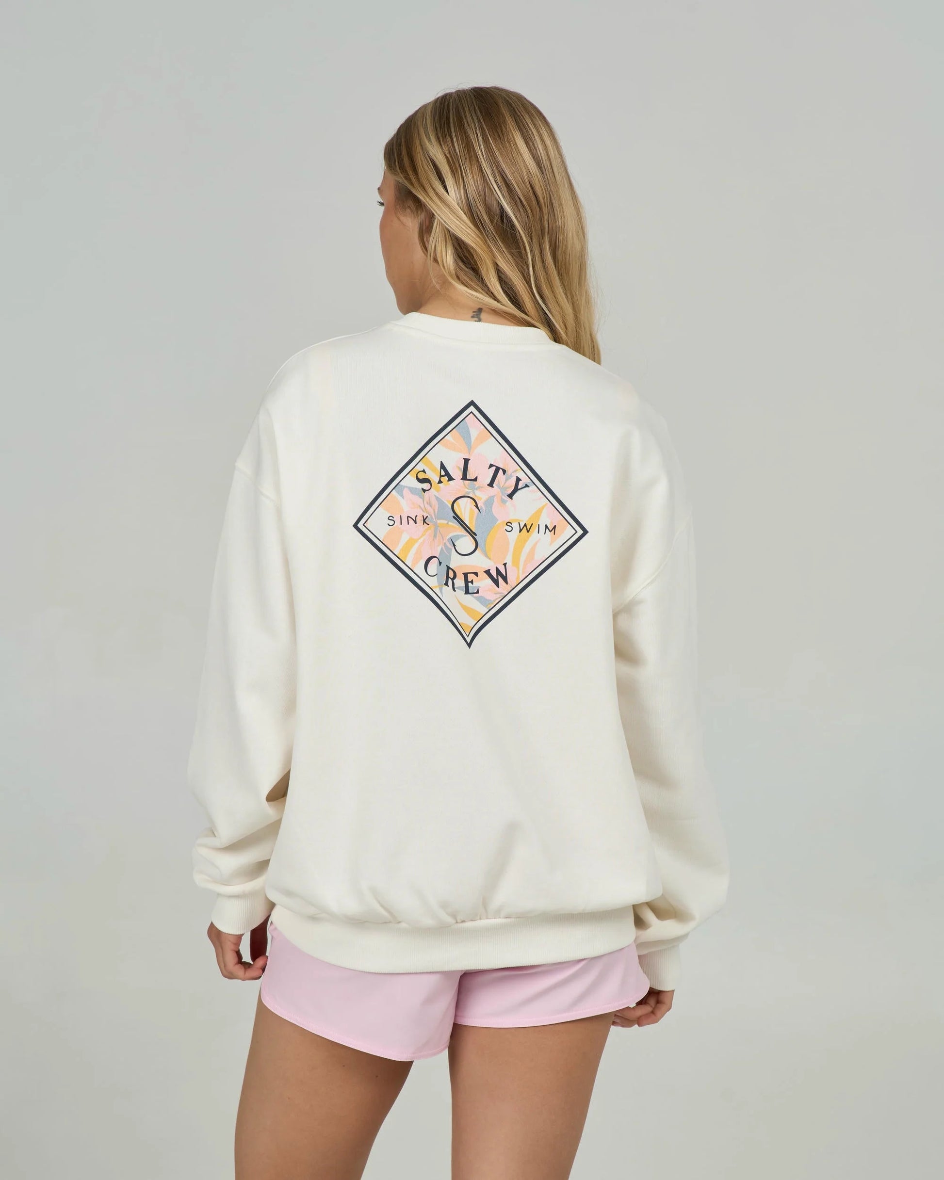 Person wearing a cream sweatshirt with a colorful logo on the back, standing against a plain background.
