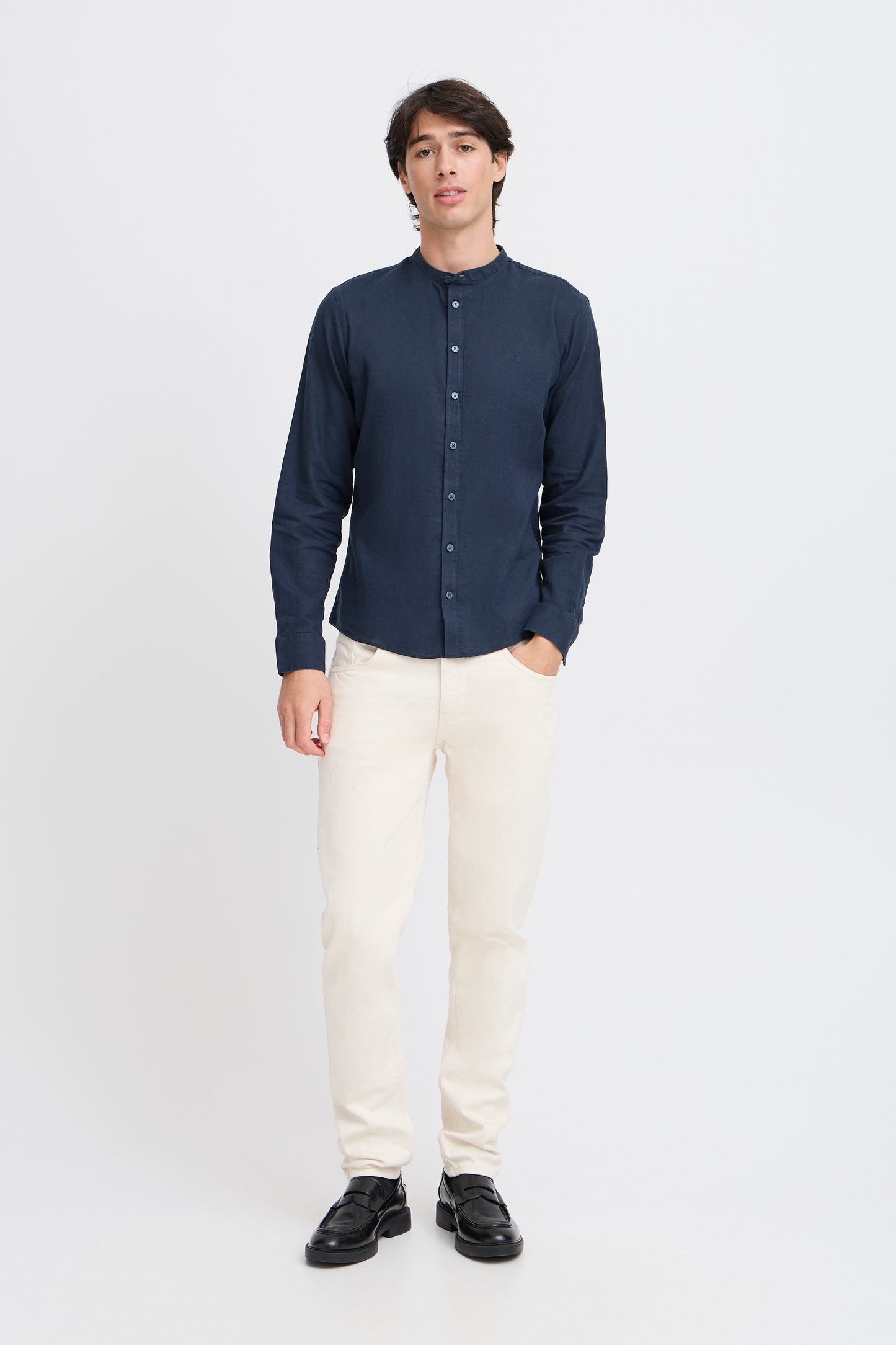 Man wearing a navy button-up shirt, white pants, and black shoes on a white background