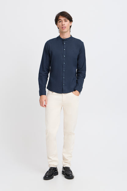 Man wearing a navy button-up shirt, white pants, and black shoes on a white background