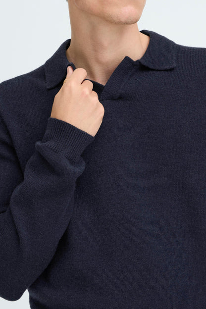 Close-up of a person wearing a dark navy knit polo sweater, with the hand adjusting the collar.