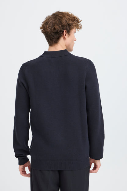 A man viewed from the back wearing a dark navy long-sleeve knit sweater and matching dark trousers against a light gray studio background.