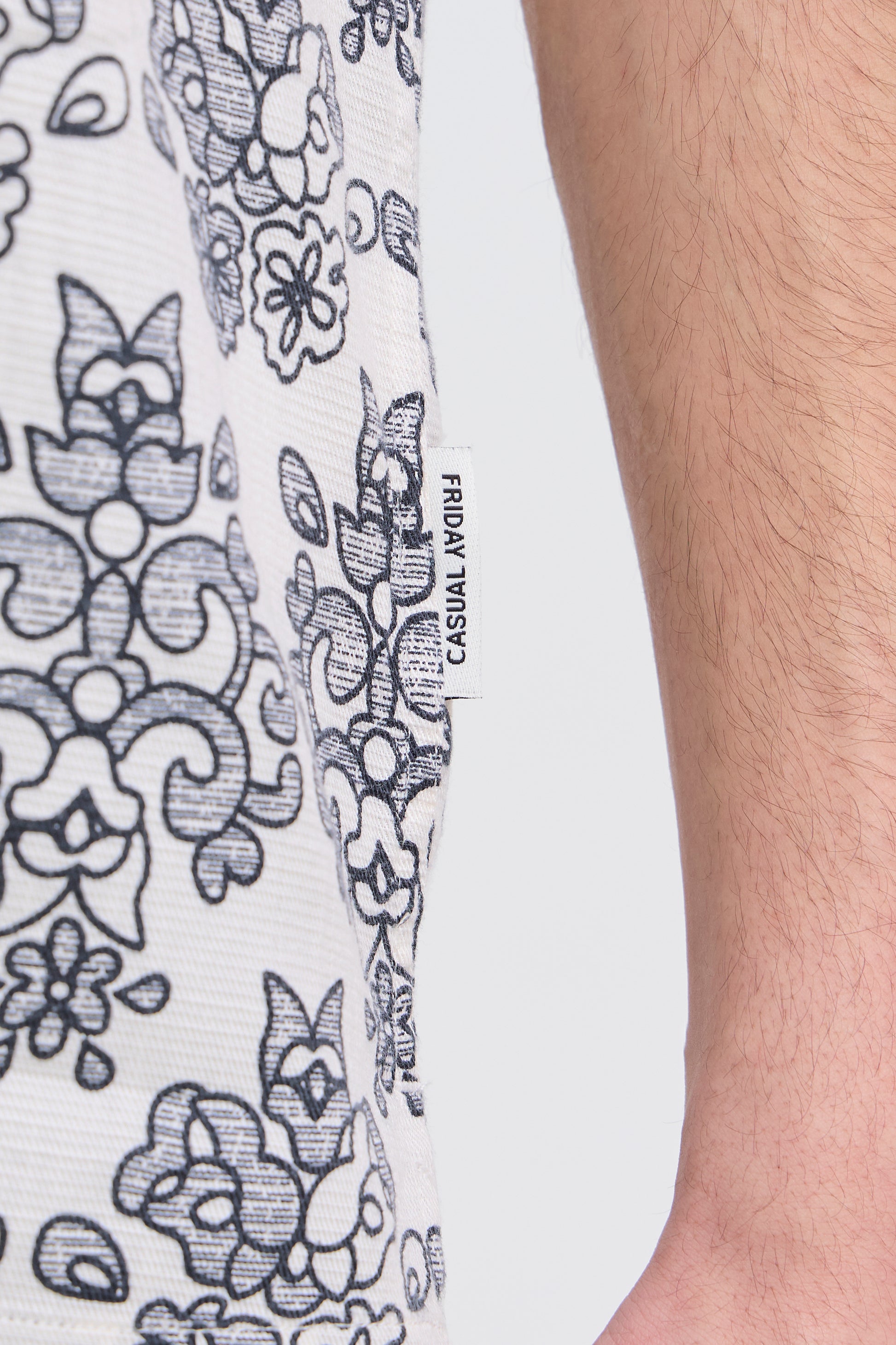 Close-up of a white garment with black floral patterns and 'Casual Aviary' branding.