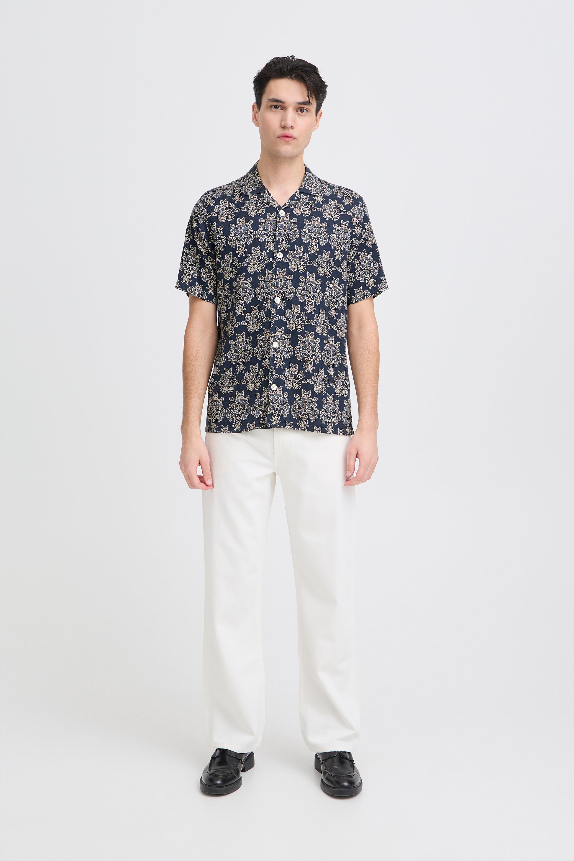 Man wearing a patterned shirt and white pants on a white background