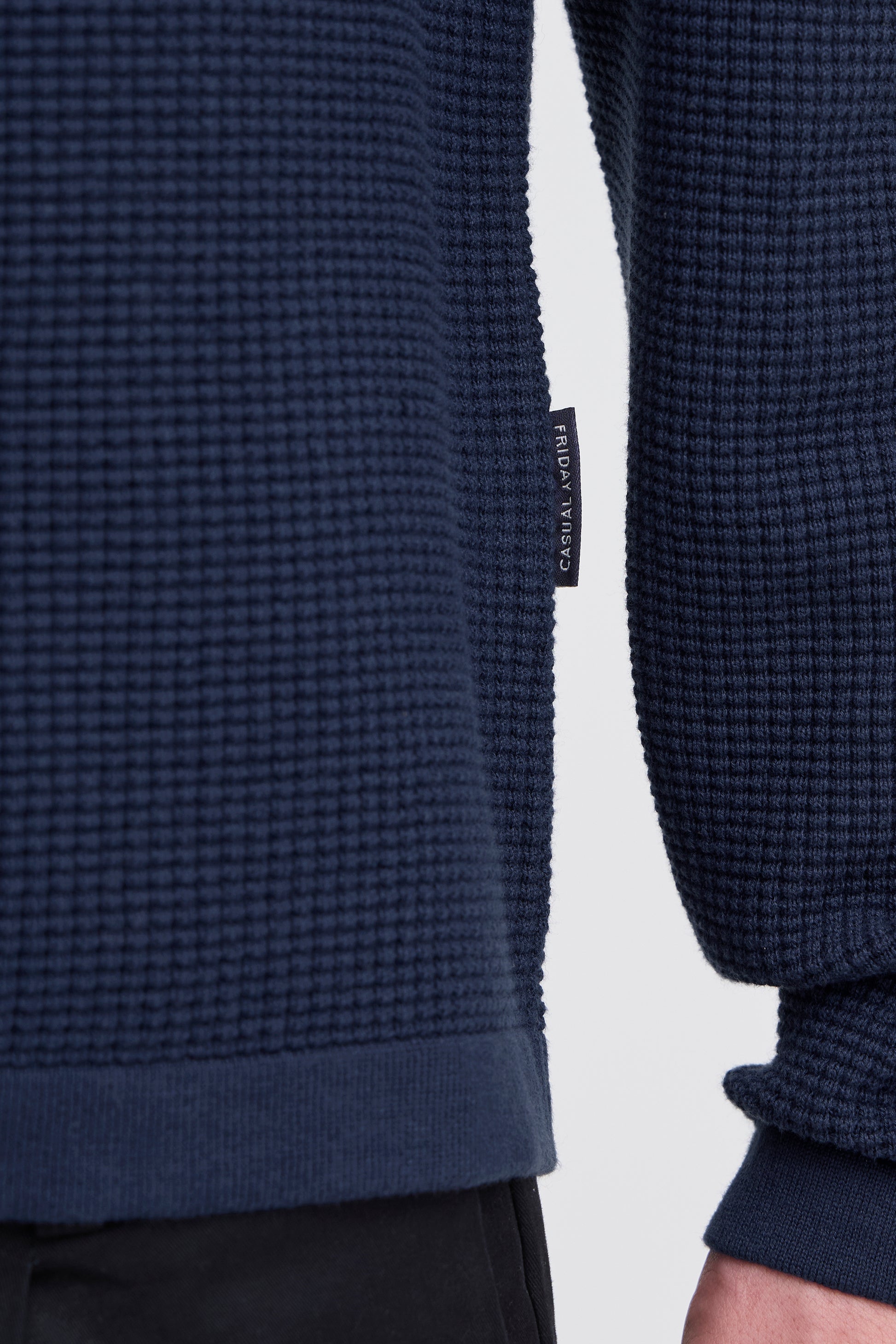 Navy textured sweater with a brand tag on a light gray background