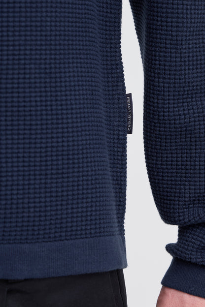 Navy textured sweater with a brand tag on a light gray background