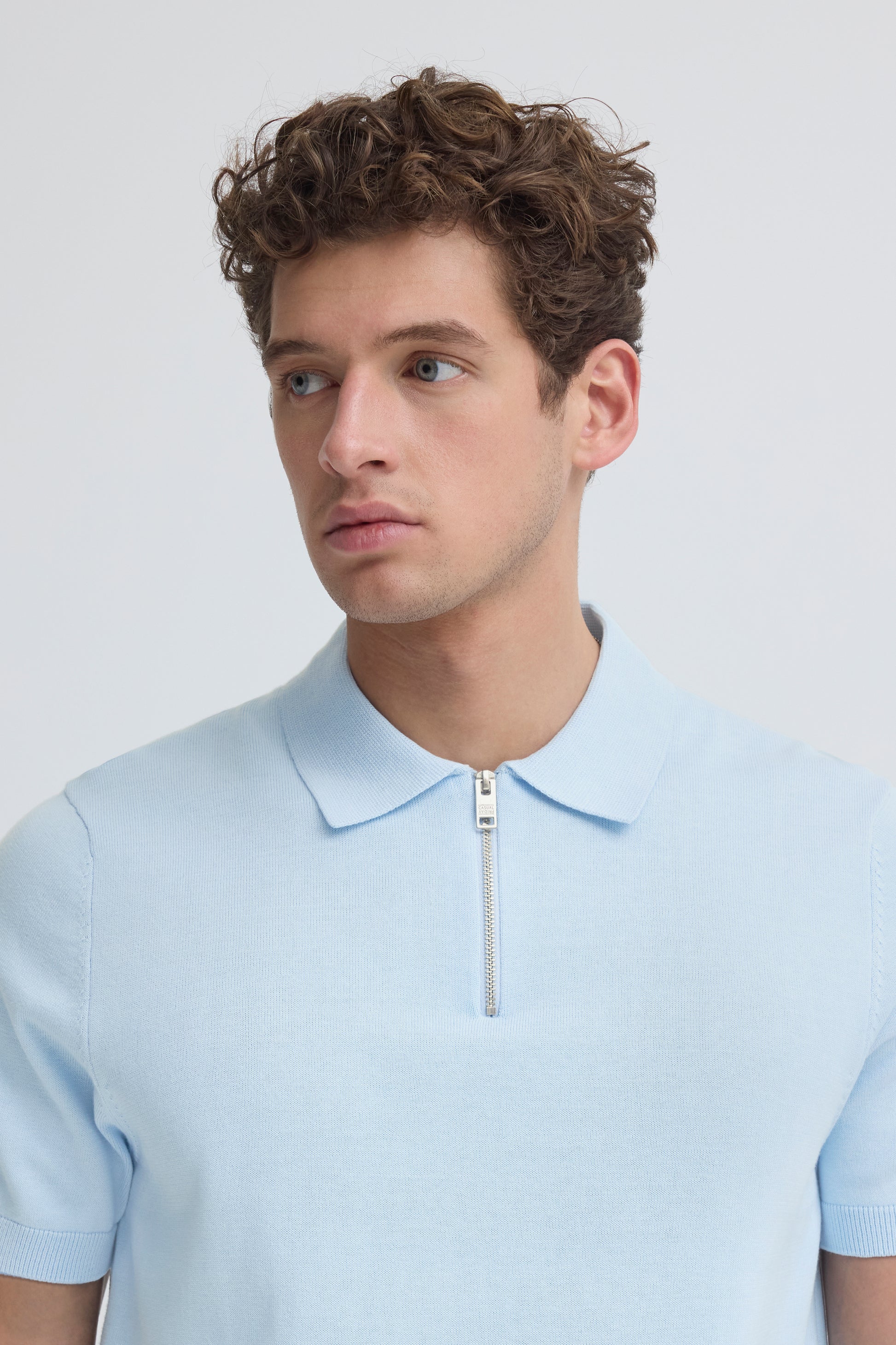 Man wearing a light blue polo shirt with a zipper on a plain background
