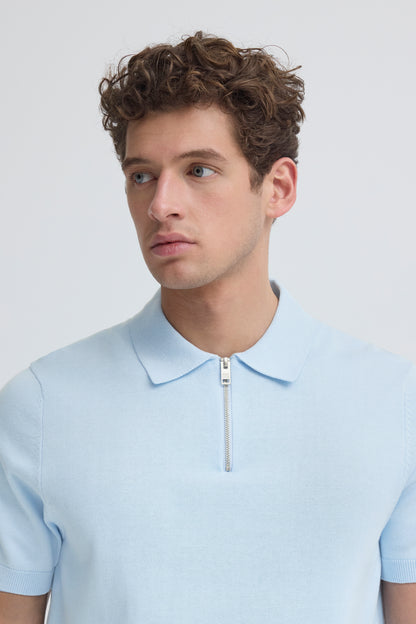 Man wearing a light blue polo shirt with a zipper on a plain background