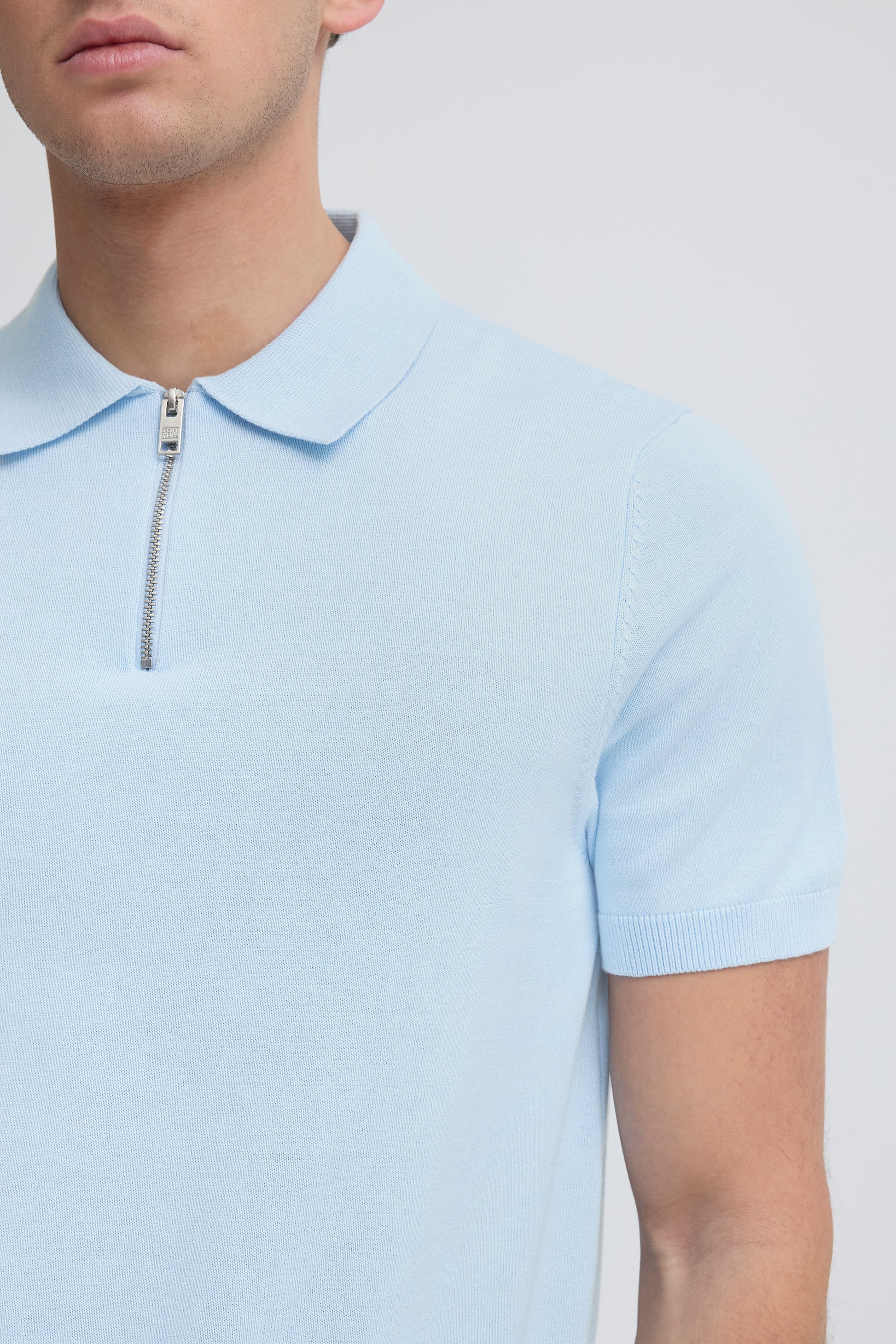 Light blue polo shirt with a zipper detail on a neutral background