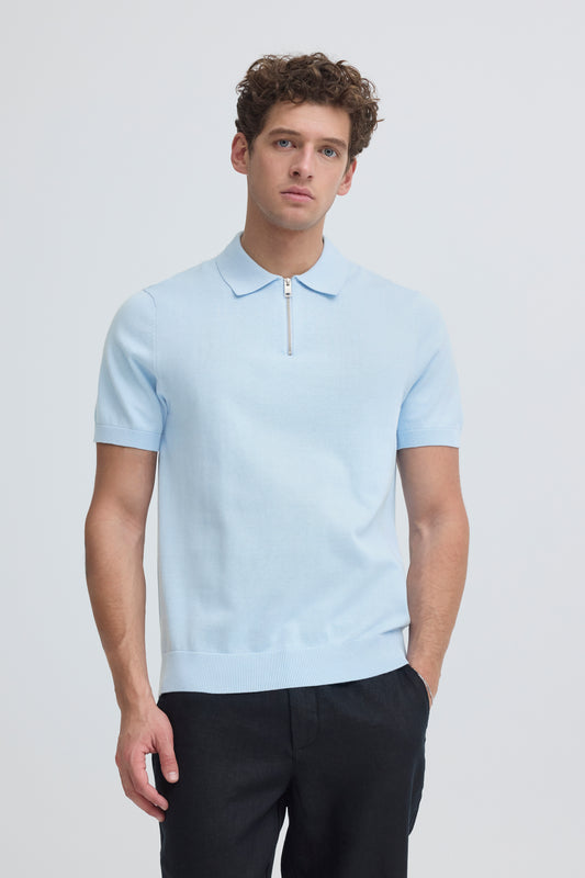 Man wearing a light blue polo shirt with a zipper on a plain background