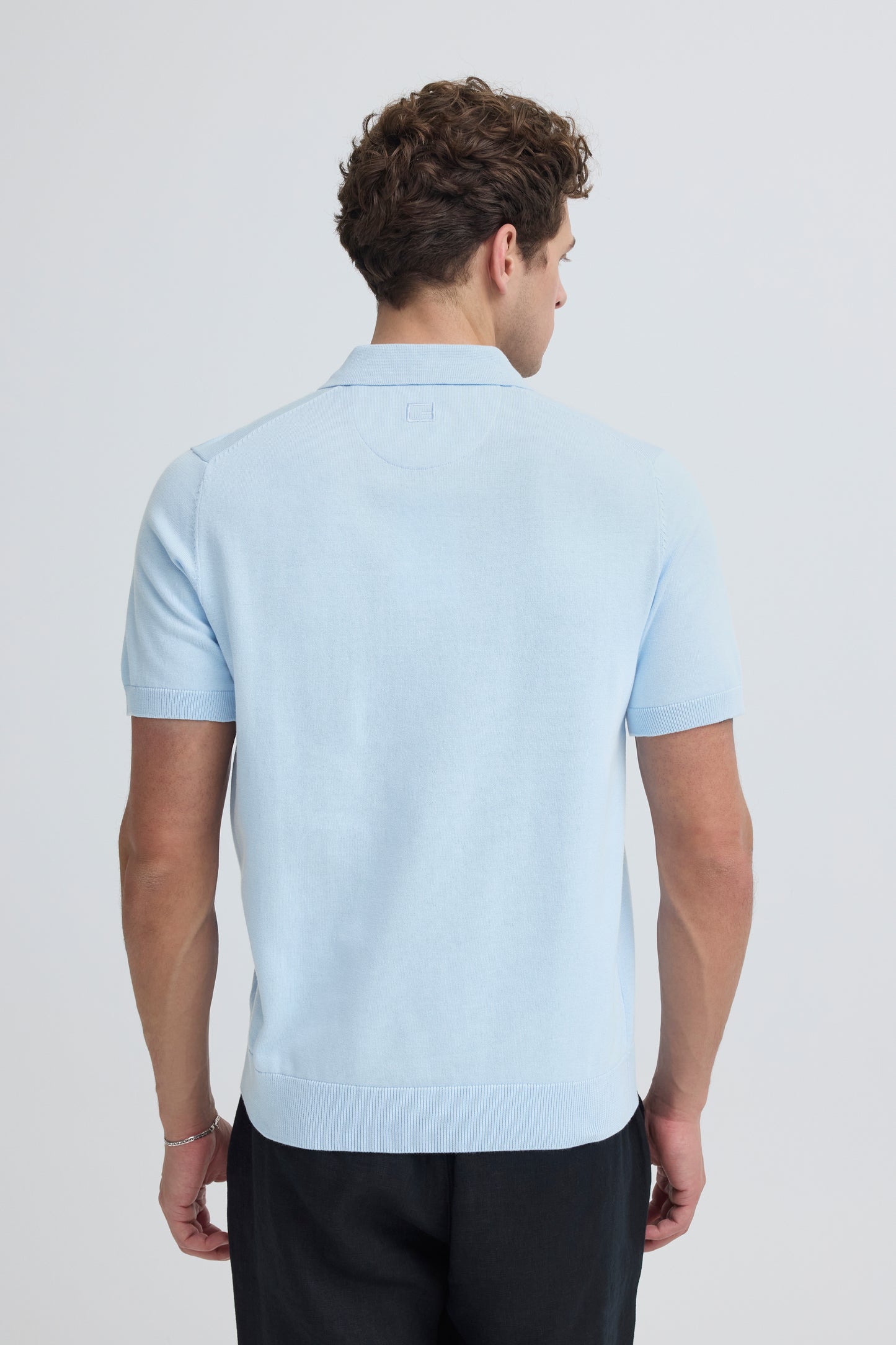 Man wearing a light blue polo shirt on a plain background