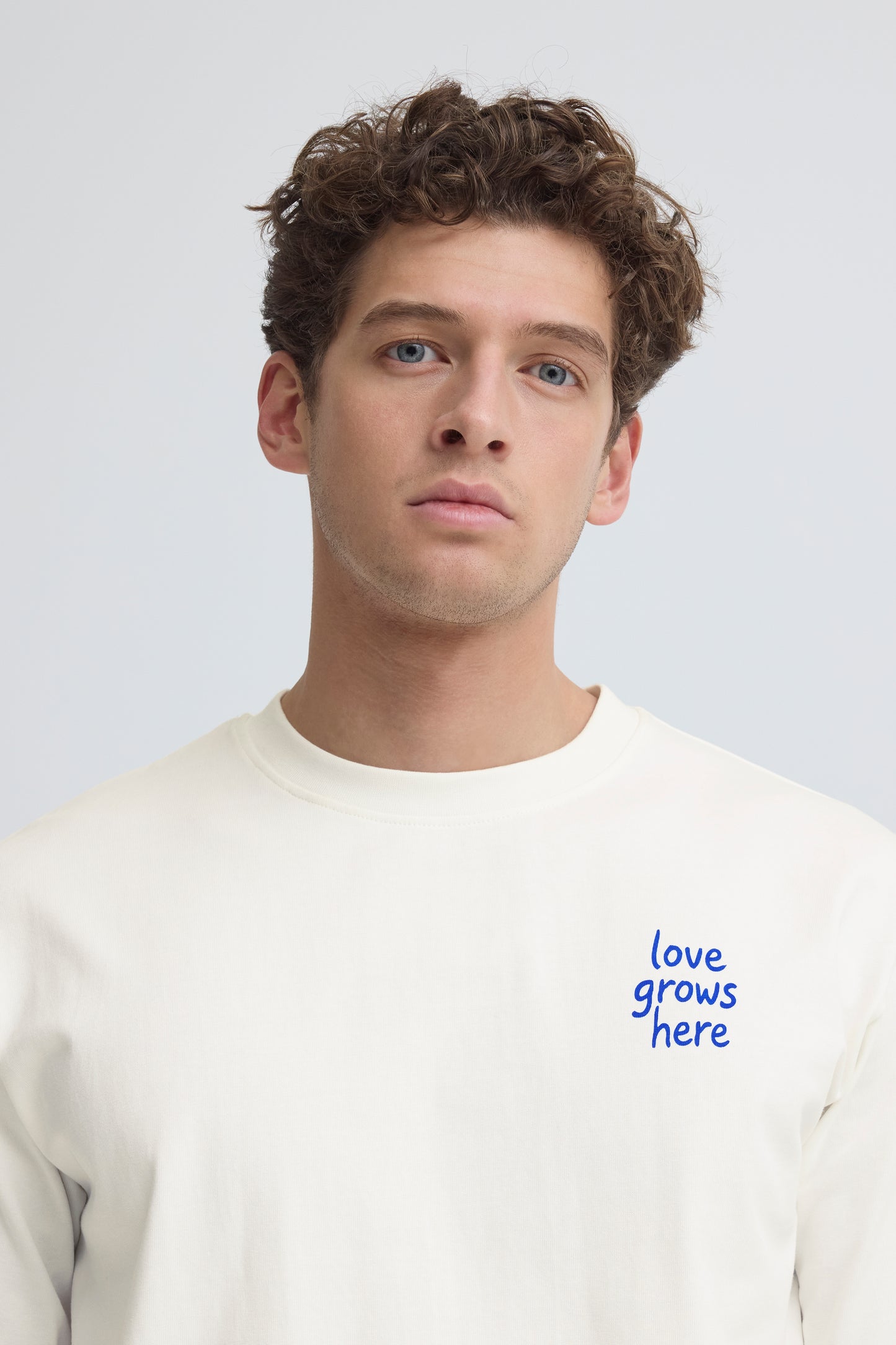 Man wearing a white sweatshirt with 'love grows here' text on a light gray background