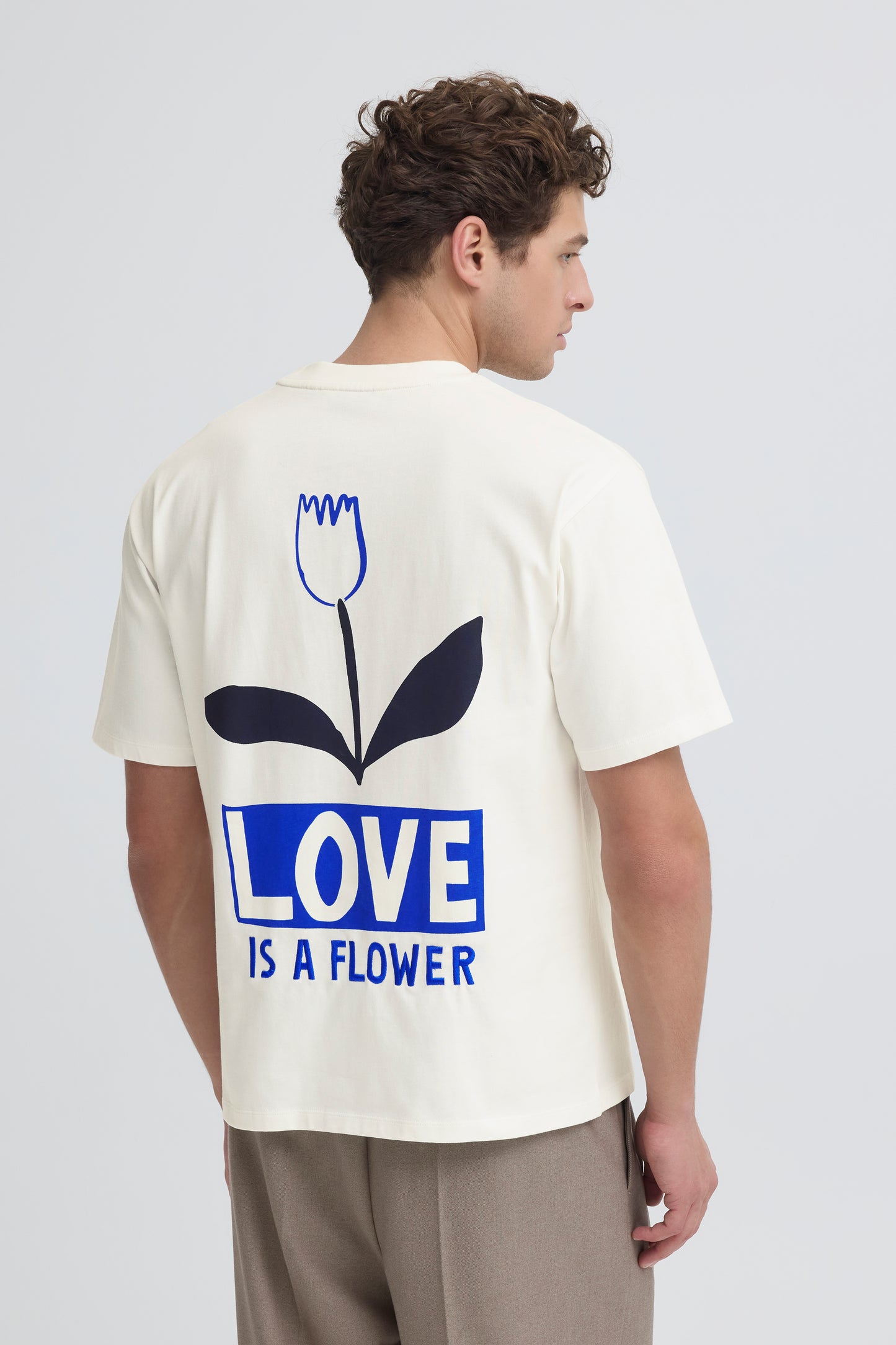 Person wearing a white t-shirt with a blue graphic and text on the back, standing against a plain background.