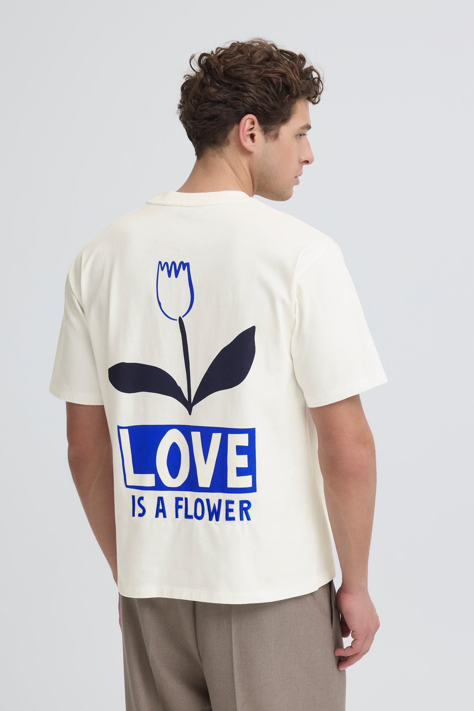 Person wearing a white t-shirt with a blue graphic and text on the back, standing against a plain background.