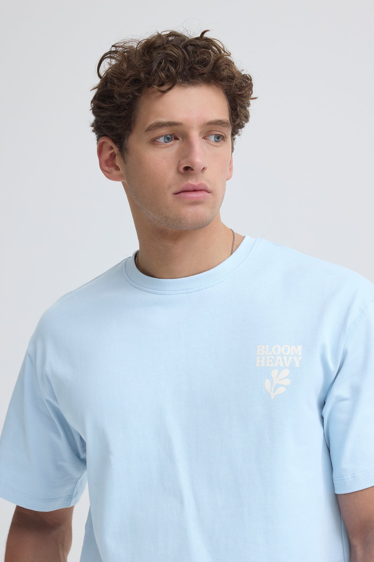 Man wearing a light blue t-shirt with a logo on a plain background